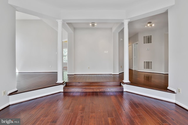 empty room with wood-type flooring, baseboards, visible vents, and ornate columns