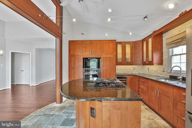 kitchen featuring backsplash, a sink, a kitchen island, dark stone counters, and glass insert cabinets
