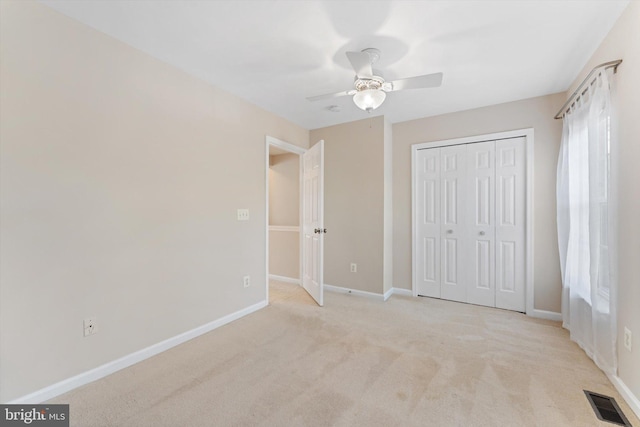unfurnished bedroom featuring ceiling fan, light colored carpet, baseboards, visible vents, and a closet
