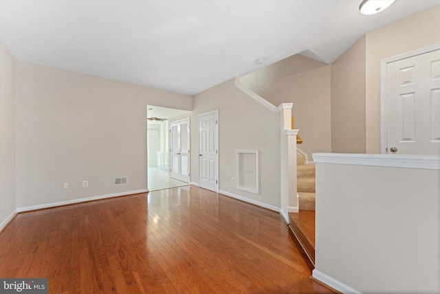 empty room with stairway, baseboards, wood finished floors, and visible vents