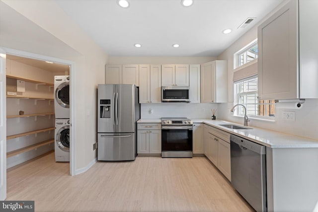 kitchen featuring light wood-type flooring, a sink, appliances with stainless steel finishes, and stacked washer / drying machine