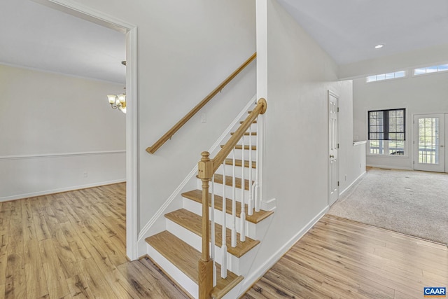 staircase featuring a chandelier, wood finished floors, a towering ceiling, and baseboards