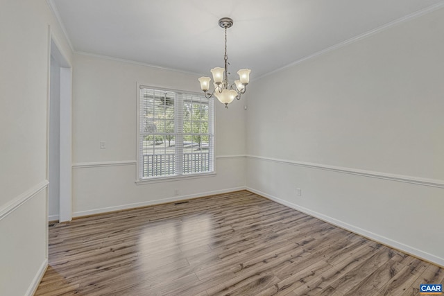 empty room with baseboards, wood finished floors, a notable chandelier, and crown molding