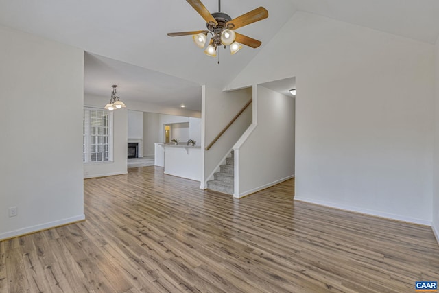 unfurnished living room featuring high vaulted ceiling, stairs, light wood-type flooring, ceiling fan, and baseboards