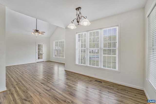 unfurnished dining area with wood finished floors, ceiling fan with notable chandelier, baseboards, lofted ceiling, and visible vents