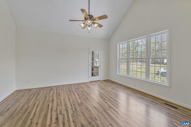 empty room with wood finished floors, visible vents, a ceiling fan, and high vaulted ceiling