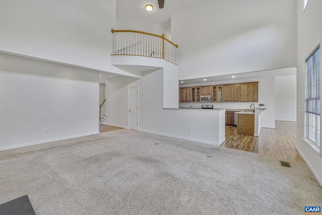 unfurnished living room with light carpet, visible vents, a high ceiling, and baseboards