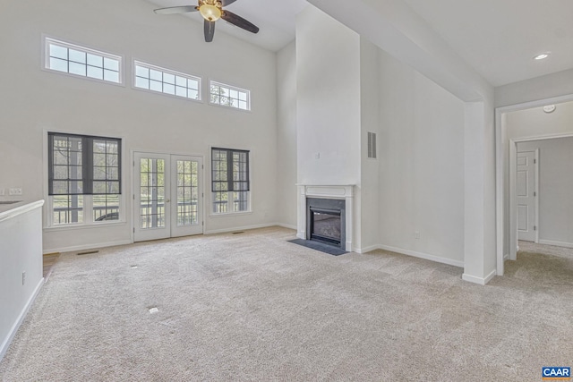 unfurnished living room with a fireplace with flush hearth, ceiling fan, carpet floors, a towering ceiling, and visible vents