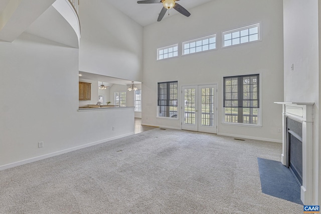 unfurnished living room featuring a fireplace with flush hearth, a wealth of natural light, a towering ceiling, and ceiling fan with notable chandelier