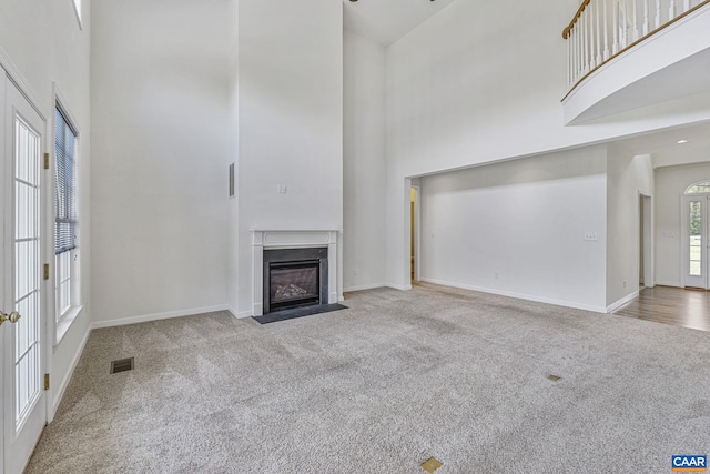 unfurnished living room featuring a high ceiling, a fireplace with flush hearth, carpet, baseboards, and visible vents
