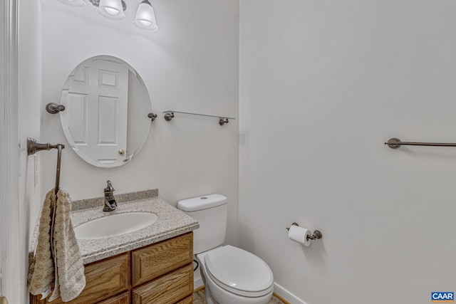 half bathroom featuring baseboards, toilet, and vanity