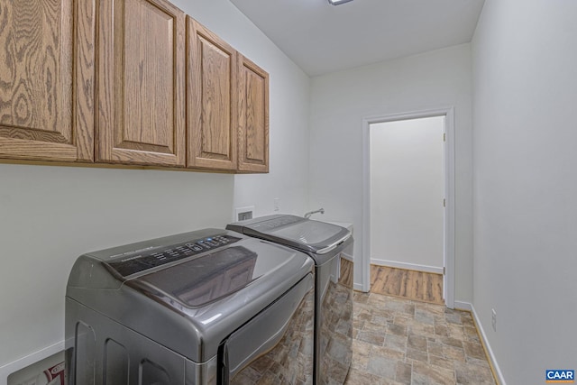 clothes washing area featuring cabinet space, stone finish flooring, baseboards, and separate washer and dryer