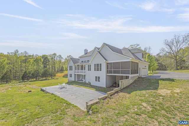 back of house with a chimney, a patio area, an attached garage, a yard, and a sunroom