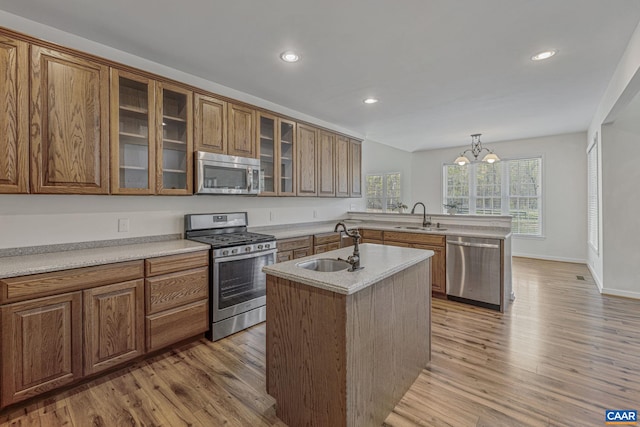 kitchen featuring light wood finished floors, a peninsula, a sink, and appliances with stainless steel finishes