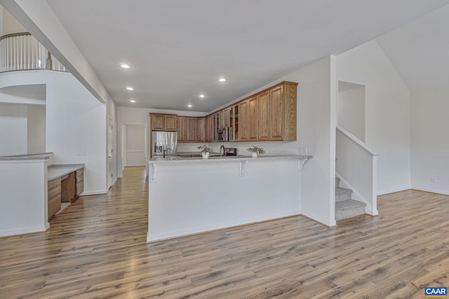 kitchen with brown cabinets, recessed lighting, stainless steel appliances, a peninsula, and light wood-style flooring