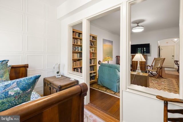 interior space featuring arched walkways, ornamental molding, built in shelves, and light wood-style floors