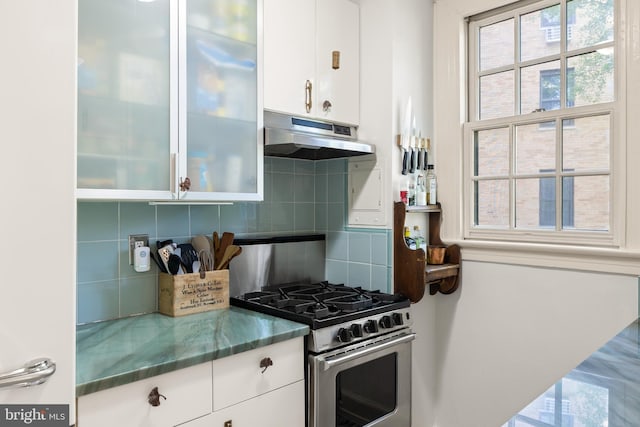 kitchen with stone countertops, white cabinetry, under cabinet range hood, tasteful backsplash, and gas stove