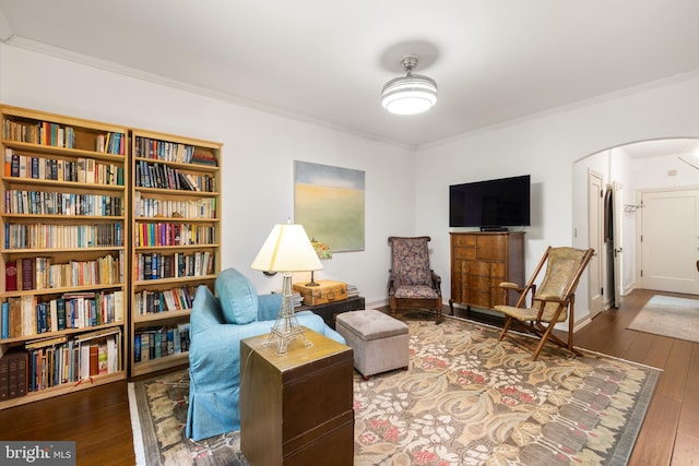 living area featuring baseboards, arched walkways, hardwood / wood-style flooring, and ornamental molding