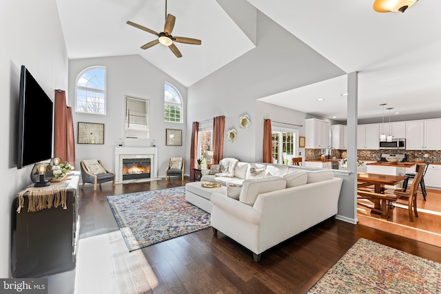 living area featuring a glass covered fireplace, a wealth of natural light, high vaulted ceiling, and ceiling fan