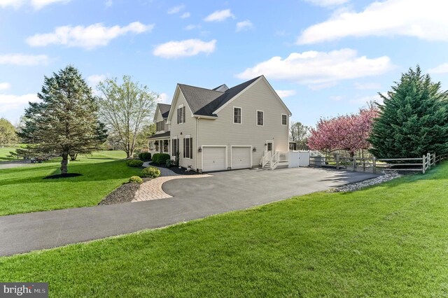 view of side of home with a lawn, an attached garage, fence, and aphalt driveway