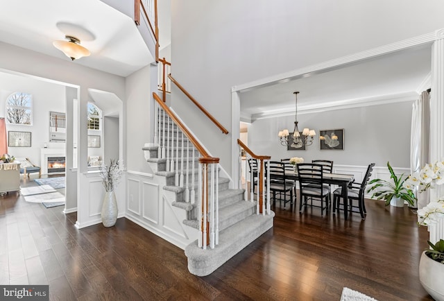 stairway featuring a chandelier, a glass covered fireplace, wood finished floors, and a decorative wall