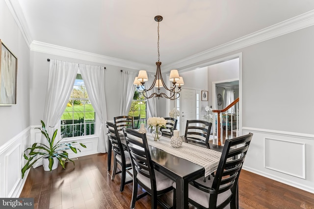 dining space featuring dark wood-style floors, wainscoting, an inviting chandelier, a decorative wall, and ornamental molding