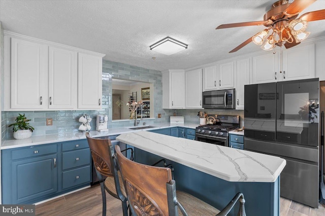 kitchen with appliances with stainless steel finishes, blue cabinets, a sink, light wood-style floors, and a breakfast bar area
