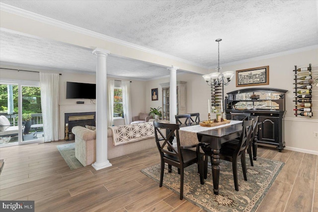 dining space with a textured ceiling, ornate columns, wood finished floors, a glass covered fireplace, and crown molding