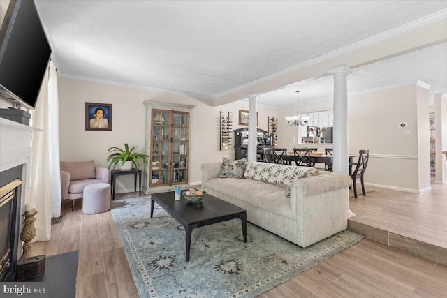 living area featuring ornate columns, wood finished floors, a glass covered fireplace, a chandelier, and crown molding
