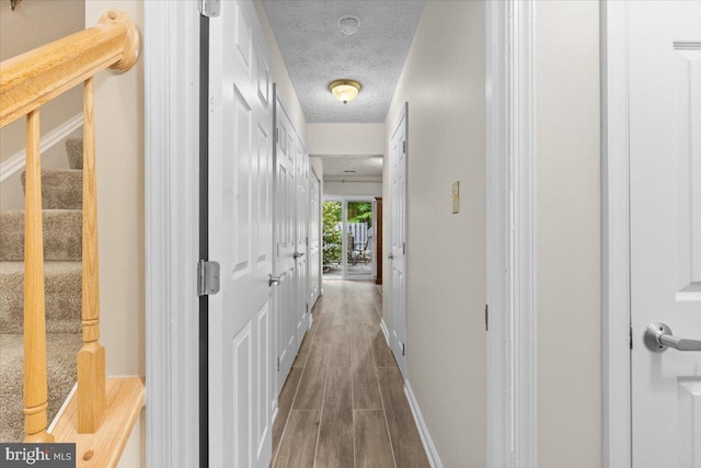 hall featuring wood finished floors, stairway, a textured ceiling, and baseboards