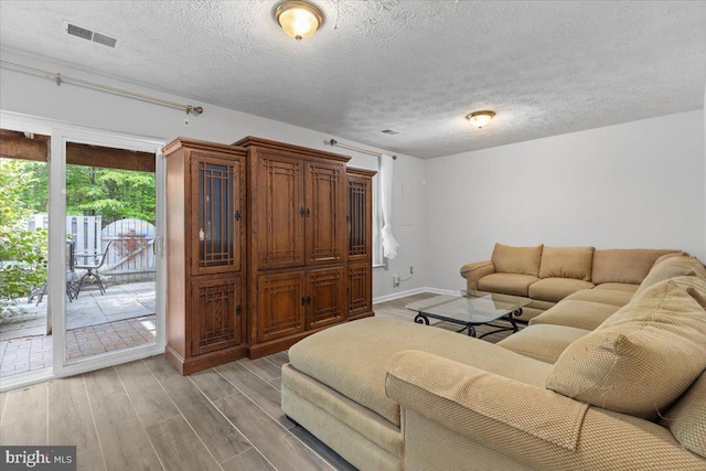 living area featuring light wood finished floors, a textured ceiling, and baseboards
