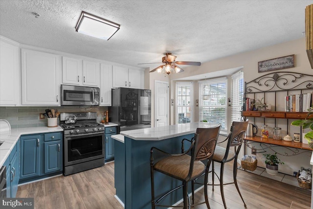 kitchen with appliances with stainless steel finishes, blue cabinetry, light wood finished floors, backsplash, and a textured ceiling