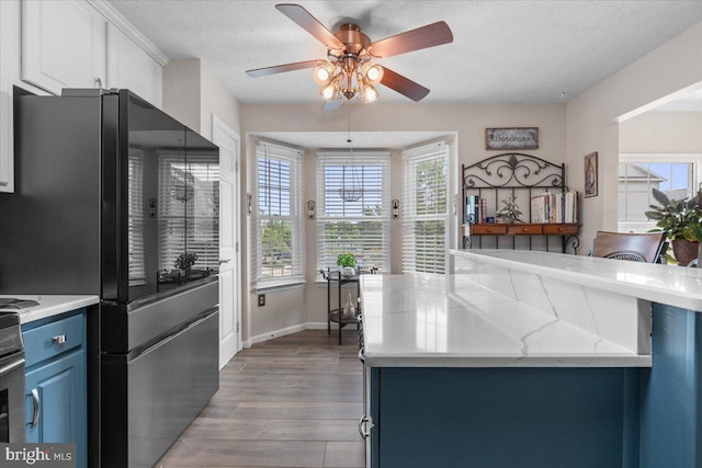 kitchen with freestanding refrigerator, ceiling fan, blue cabinets, wood finished floors, and white cabinetry
