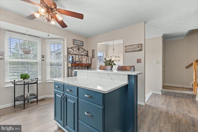 kitchen featuring blue cabinets, light wood-style flooring, a ceiling fan, light countertops, and a textured ceiling