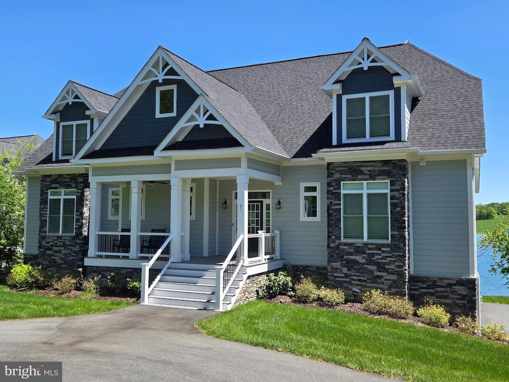 craftsman inspired home with a porch, a shingled roof, and stone siding