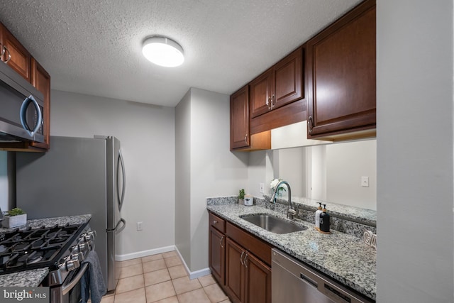 kitchen featuring light tile patterned flooring, light stone countertops, a textured ceiling, a sink, and appliances with stainless steel finishes