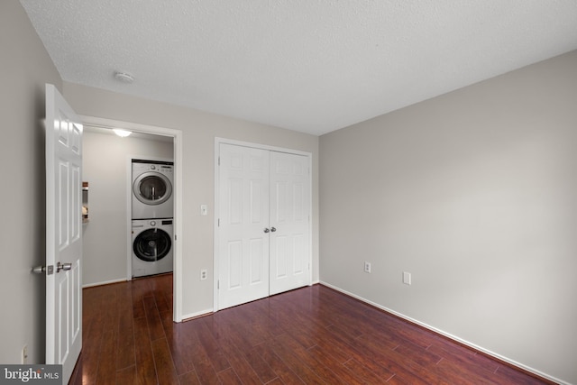 unfurnished bedroom with a closet, stacked washer and dryer, baseboards, and wood finished floors