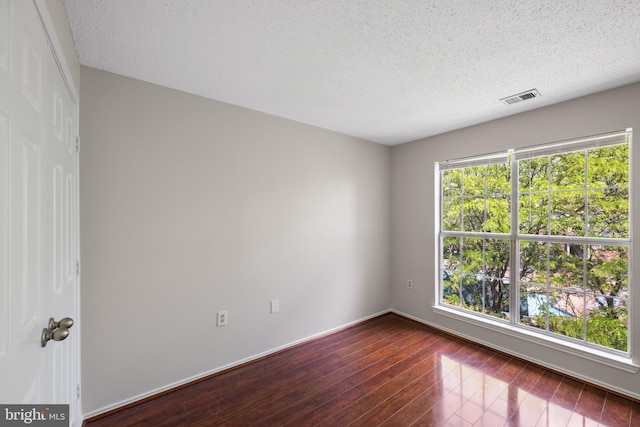 spare room with a textured ceiling, visible vents, baseboards, and dark wood-type flooring