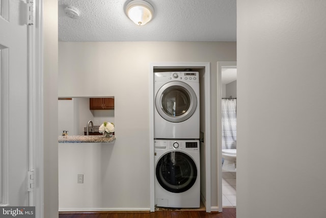 washroom with laundry area, stacked washer and clothes dryer, a textured ceiling, and wood finished floors
