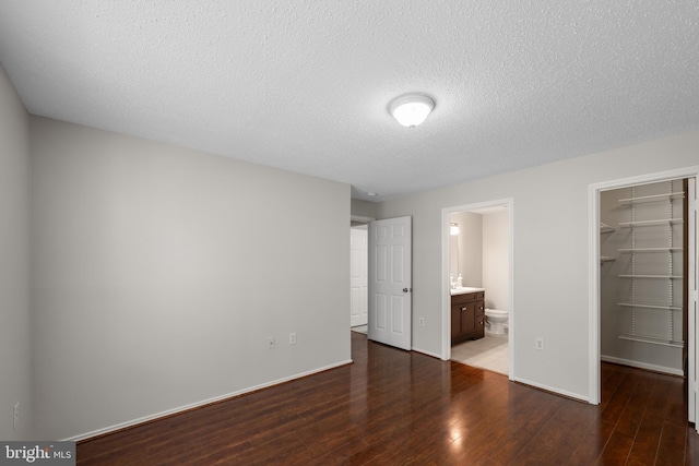 unfurnished bedroom featuring a closet, wood finished floors, baseboards, a walk in closet, and a textured ceiling