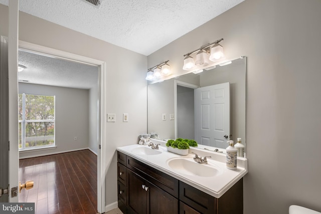 bathroom with a sink, double vanity, a textured ceiling, and wood finished floors