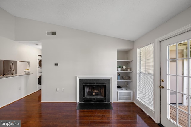 unfurnished living room with stacked washer / drying machine, visible vents, wood finished floors, and vaulted ceiling