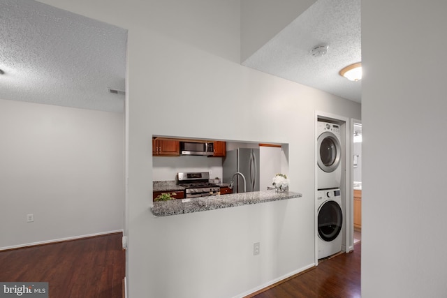 clothes washing area with laundry area, a textured ceiling, stacked washing maching and dryer, visible vents, and dark wood-style floors