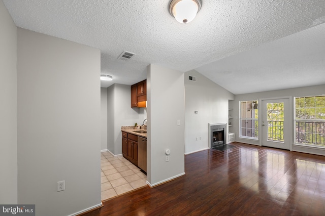 unfurnished living room with a sink, a fireplace with flush hearth, light wood-style flooring, and visible vents