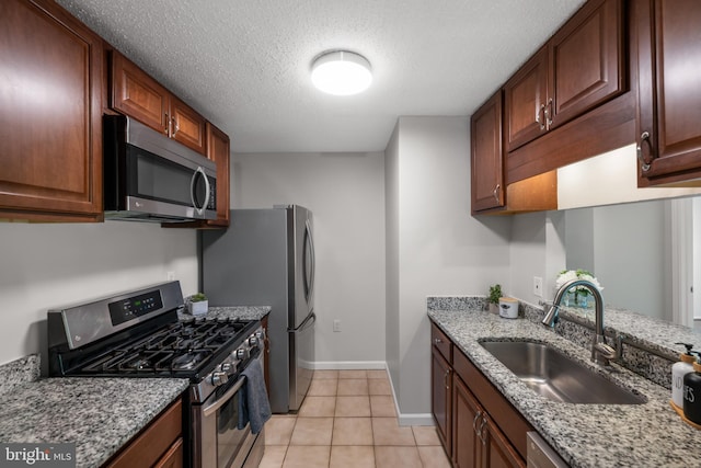 kitchen with light stone countertops, baseboards, a textured ceiling, a sink, and appliances with stainless steel finishes