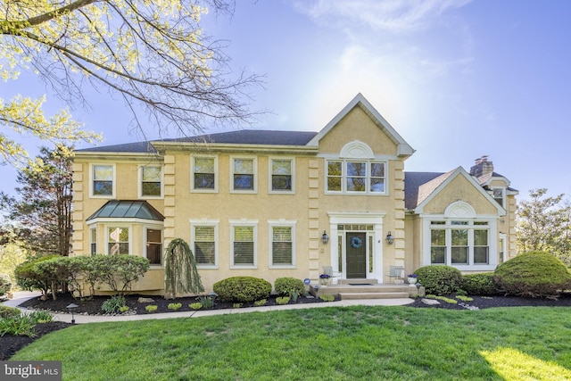 view of front of home featuring stucco siding, a chimney, and a front lawn