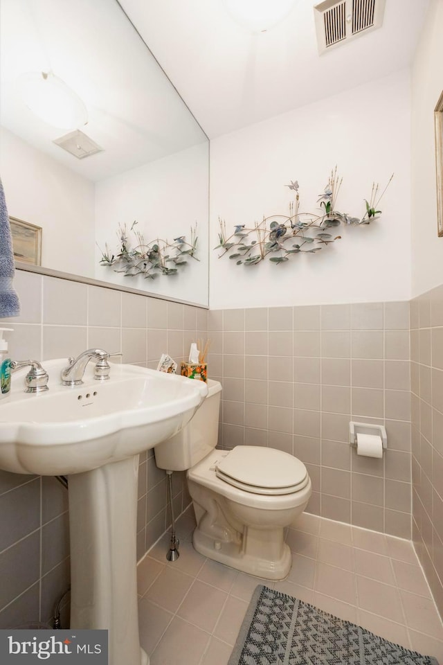 half bathroom featuring tile patterned flooring, visible vents, toilet, and tile walls