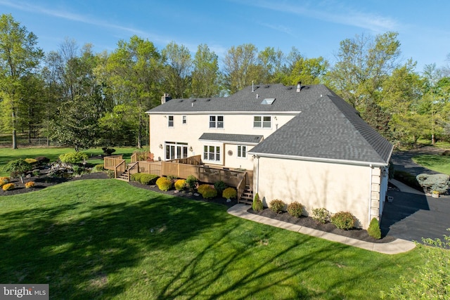 back of house with a wooden deck, roof with shingles, stucco siding, a chimney, and a lawn