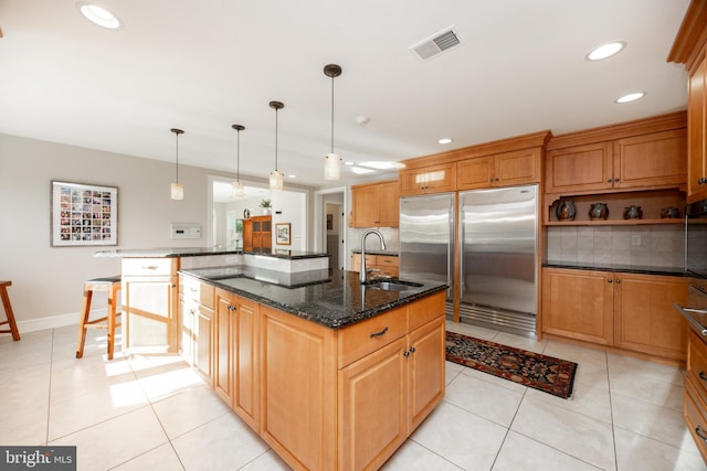 kitchen with visible vents, tasteful backsplash, a sink, built in refrigerator, and an island with sink
