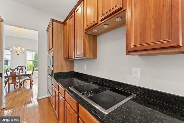 17435 Lethridge Cir, Round Hill, VA 20141 - kitchen with black electric cooktop, a chandelier, brown cabinets, light wood-style flooring, and dark stone counters